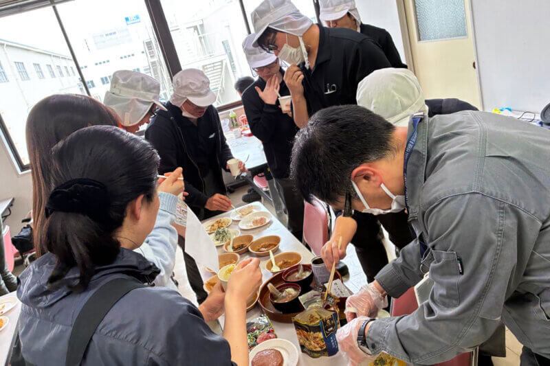 防災備蓄品のおでんやパスタを手に取る社員の写真